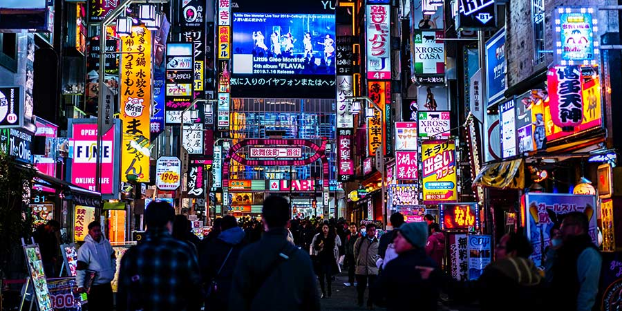 The streets of Tokyo lit up at night with many colourful advertising screens. 