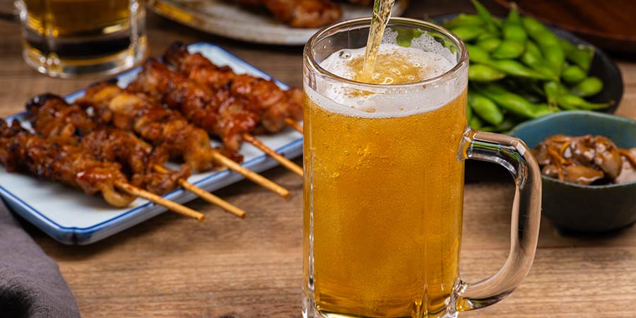 A traditional izakaya meal consisting of skewered meats, edamame, pickles and a Japanese beer.  