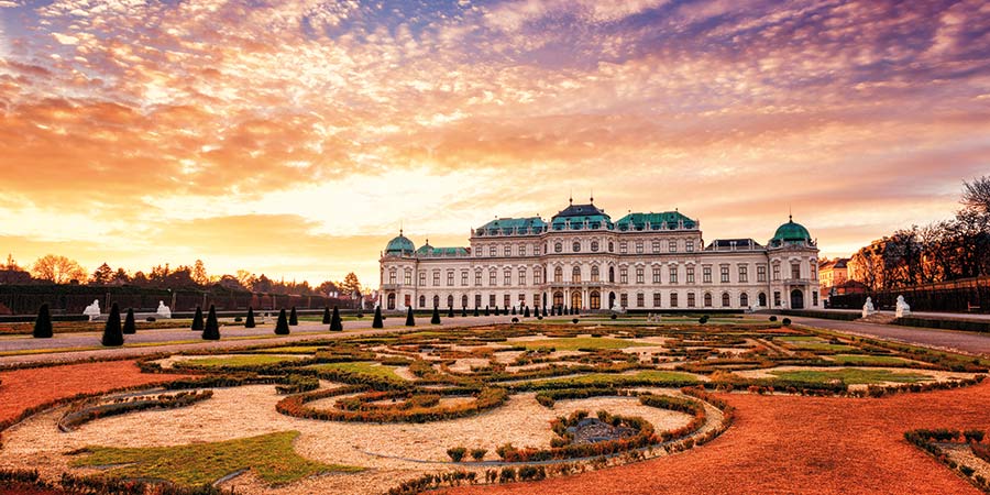 The Palace and royal gardens of Vienna are lit by a beautiful orange sunset. 